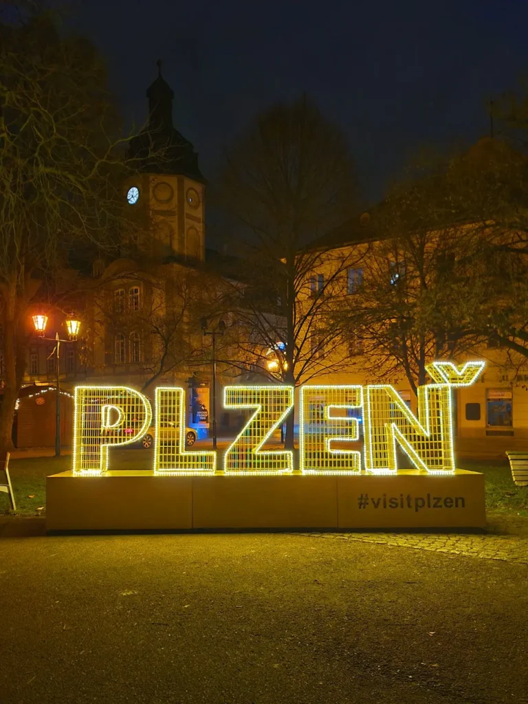 Світловий напис PLZEŇ у вечірньому місті на тлі історичних будівель